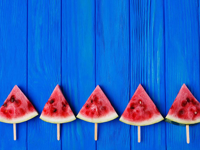 5 triangular watermelon slices with popsicle sticks pierced through the rinds