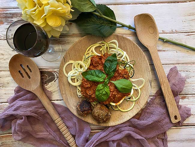 Zoodles on wooden plate with marinara sauce on top and turkey meatballs placed at edge of plate, with utensils surrounding plate on wooden table.