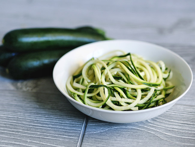 A bowl full fo zucchini noodles, also called zoodles, in a white bowl.