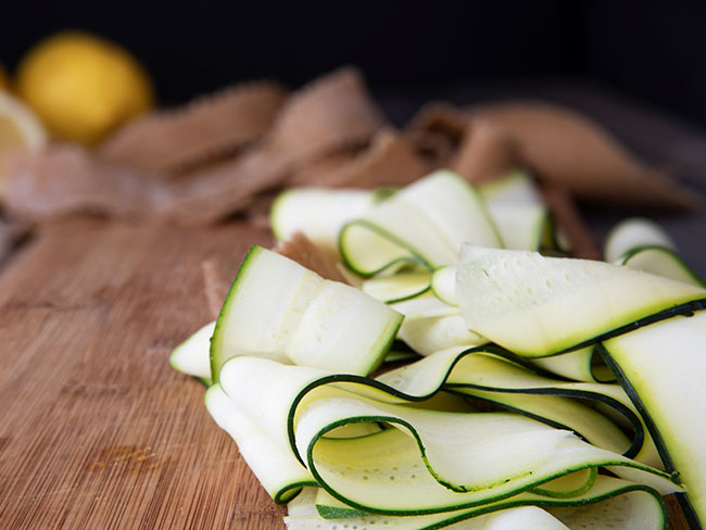 Fresh zucchini sliced into ribbons and sitting on wooden cutting board.